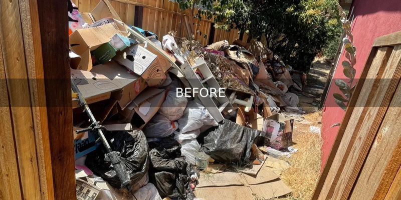 A large pile of junk filling up an alley next to a house